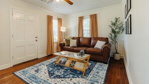 A living room with a brown leather sofa, a coffee table, a blue patterned rug, a ceiling fan, and a potted plant. - Historic Revival King Bed Liberty Bowl Memphis 895 (Memphis)
