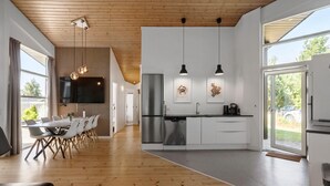 A modern kitchen with a central island, stainless steel appliances, pendant lighting, and large windows offering views of the outdoors. - Awesome home in Væggerløse with sauna (Væggerløse)