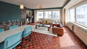 A modern living room with a dining area, large windows, and a fireplace. - 3 bedroom nice apartment in Oostende (Oostende)
