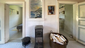 A room with a fireplace, a painting of a coastal scene, and a bucket of firewood. - 3 bedroom amazing home in Grundsund (Grundsund)