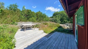 A wooden deck with a picnic table, surrounded by greenery and a building with green trim. - 3 bedroom amazing home in Grundsund (Grundsund)