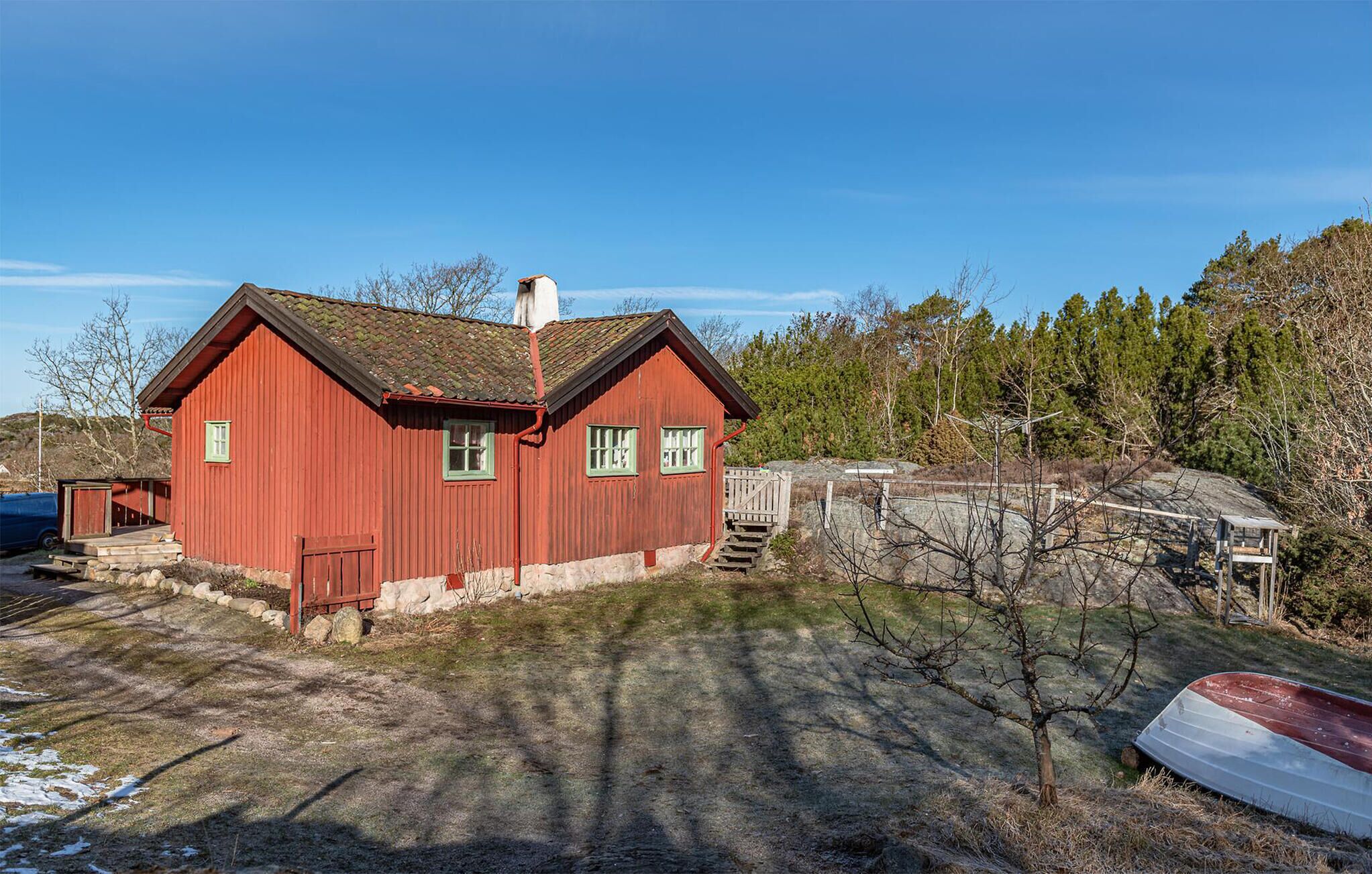 A red wooden house with a chimney, a small porch, and a boat in the background.