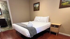 Quarto com uma cama grande, piso de madeira, mesa de cabeceira e um quadro na parede.