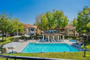 Ein Poolbereich mit Liegestühlen und Sonnenschirmen, umgeben von Gebäuden mit Balkonen.