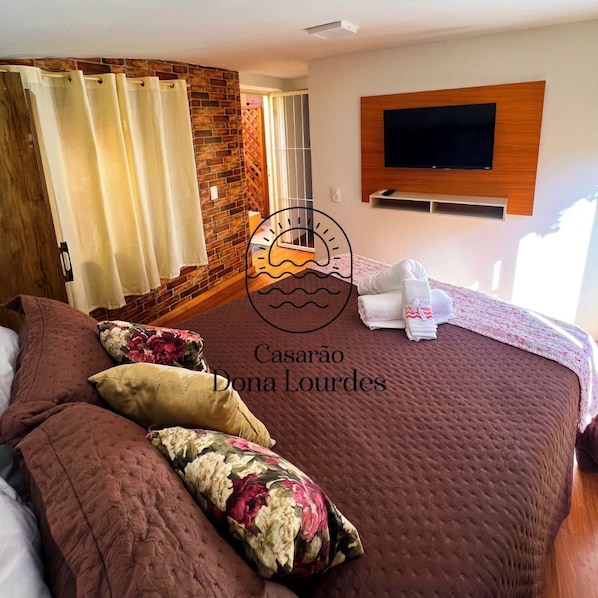 A hotel room with a large bed, a TV mounted on the wall, and a brick accent wall.