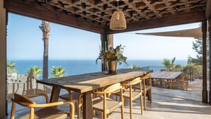 A wooden table and chairs in a covered outdoor area with a view of the ocean. - Villa 'Rocca' with Sea View, Wi-Fi and Air Conditioning (La Herradura)