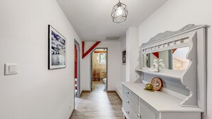 Ein Korridor mit weißer Wand, einem gerahmten Bild, einer Leuchte und einem Spiegel mit Dekoration.