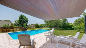 Ein Schwimmbecken mit überdachter Terrasse, inklusive Liegestühlen und einem Tisch.