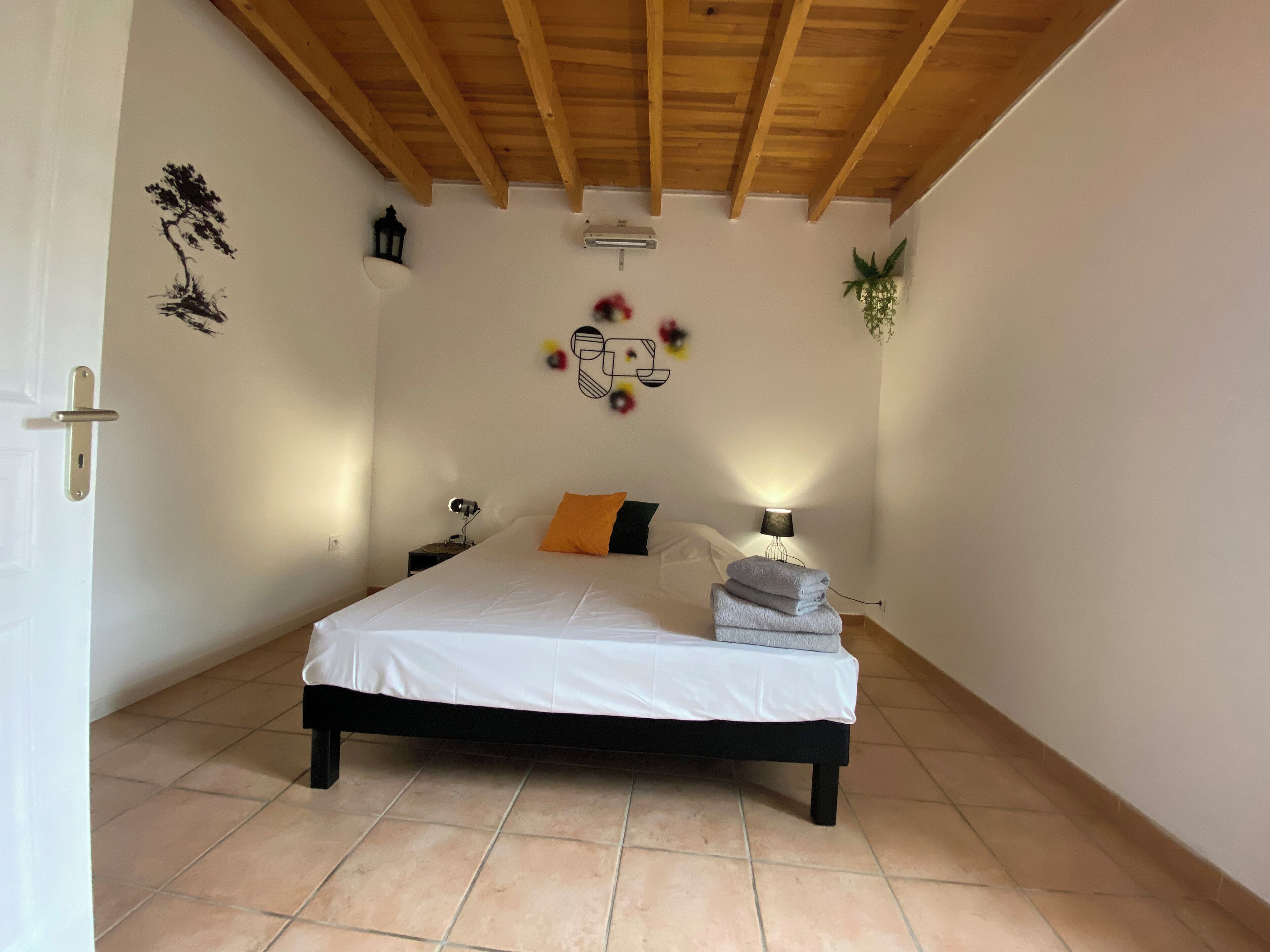 A bedroom with a bed, a nightstand, a lamp, a wall decoration, and a cross on the wall.