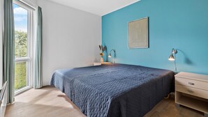 Un dormitorio con una cama grande, una ventana con cortinas, una mesita de noche con lámpara y una luz en la pared.