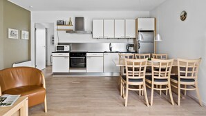 Una cocina moderna con armarios blancos, horno empotrado y comedor con sillas de madera.