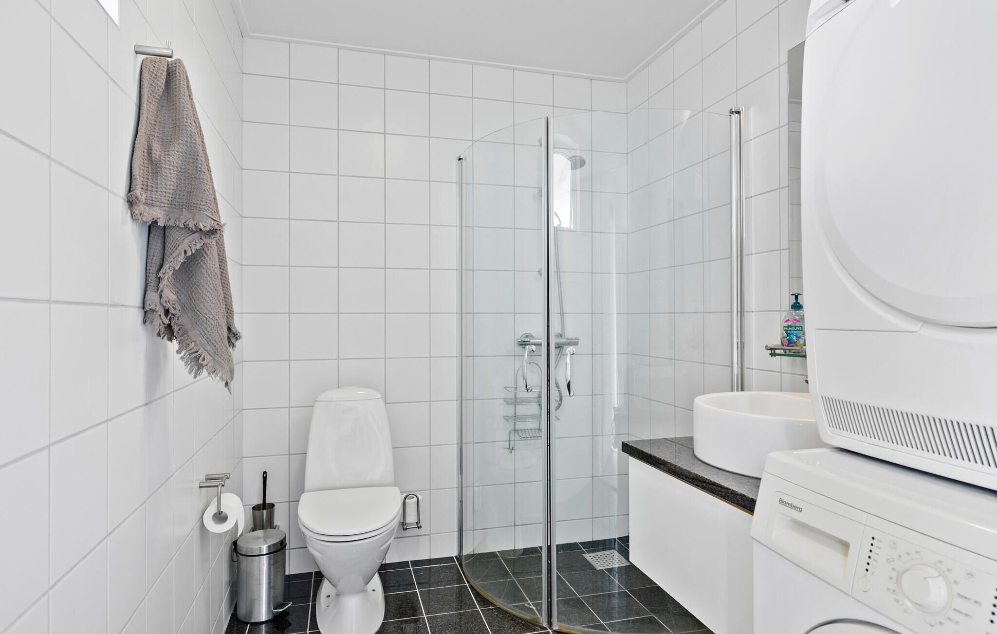 A modern bathroom with a glass-enclosed shower, a toilet, a sink, and a washing machine.