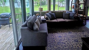 A modern living room with a sectional sofa, a patterned rug, and a large window offering a view of the backyard.