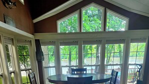 A kitchen with a wooden countertop, a dining table with chairs, and large windows offering a view of the outdoors.