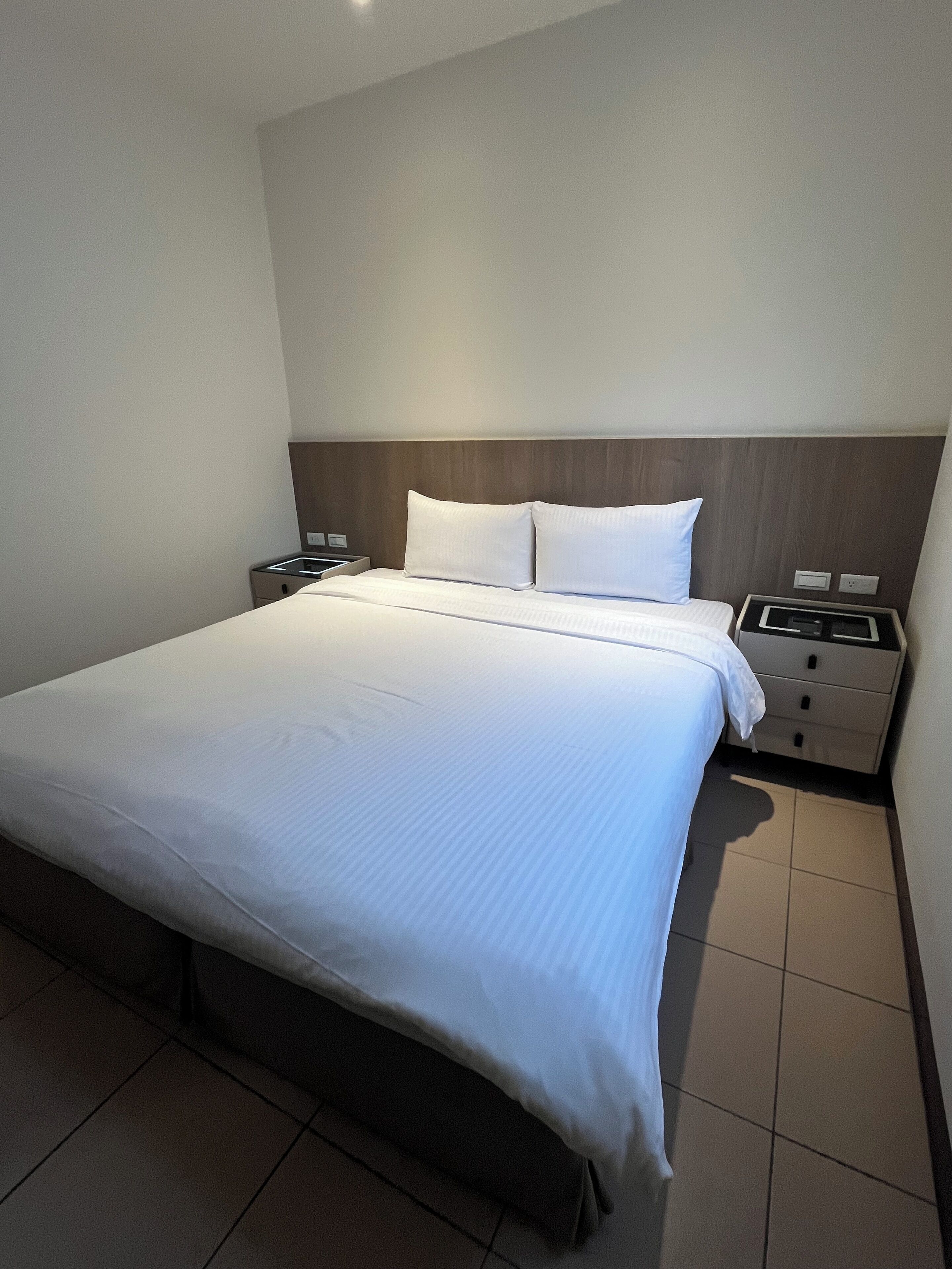 Ein Hotelzimmer mit einem großen Bett, zwei Nachttischen und einem Holzkopfteil.