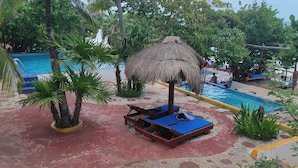 Un espace piscine avec des chaises longues et un parasol en chaume.