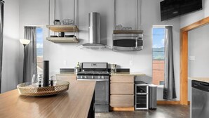 A modern kitchen with a wooden table, stainless steel appliances, and a view of the beach.