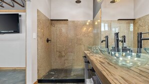 A modern bathroom with a glass vessel sink, a walk-in shower, and a mounted television.