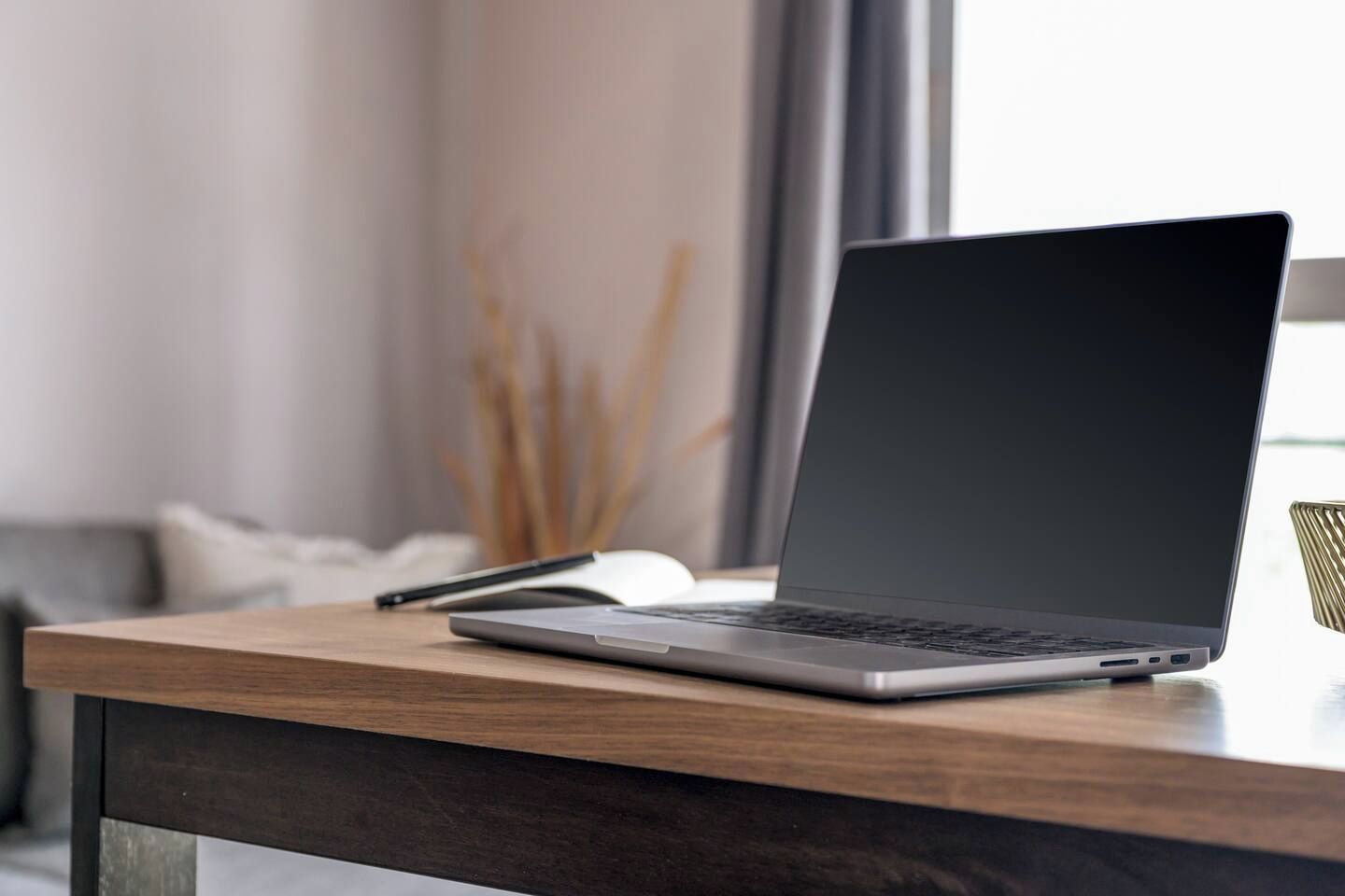 A laptop on a wooden desk with a pen and a notebook beside it.