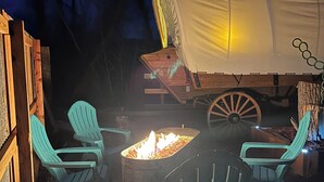 A covered camping area with a fire pit and Adirondack chairs.