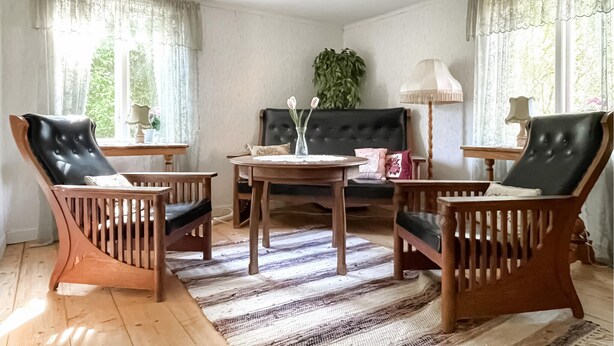 A living room with a black sofa, two wooden chairs, a round wooden table, and a striped rug. - Cozy home in Kristinehamn with WiFi (Kristinehamn)