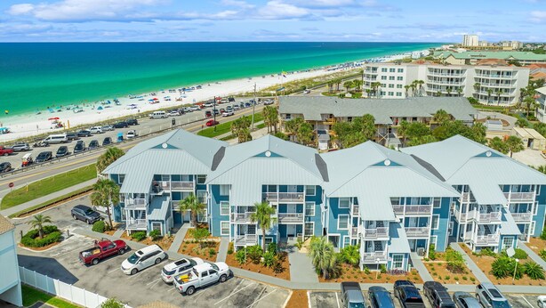 A beachfront hotel with multiple-story buildings, a parking lot, and a beach in the background. - Spring Discounts! Pool & Hot tub.1st Fl. (Miramar Beach)