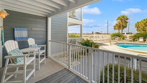 A balcony with white chairs and a table, a pool, and a view of palm trees and a parking lot. - Spring Discounts! Pool & Hot tub.1st Fl. (Miramar Beach)