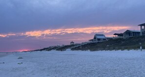 Une plage bordée d’une rangée de bâtiments, dont certains sont dotés de balcons, sous un ciel au coucher du soleil.