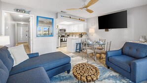 A modern living room with blue sofas, a wooden coffee table, and a TV mounted on the wall. - Spring Discounts! Pool & Hot tub.1st Fl. (Miramar Beach)