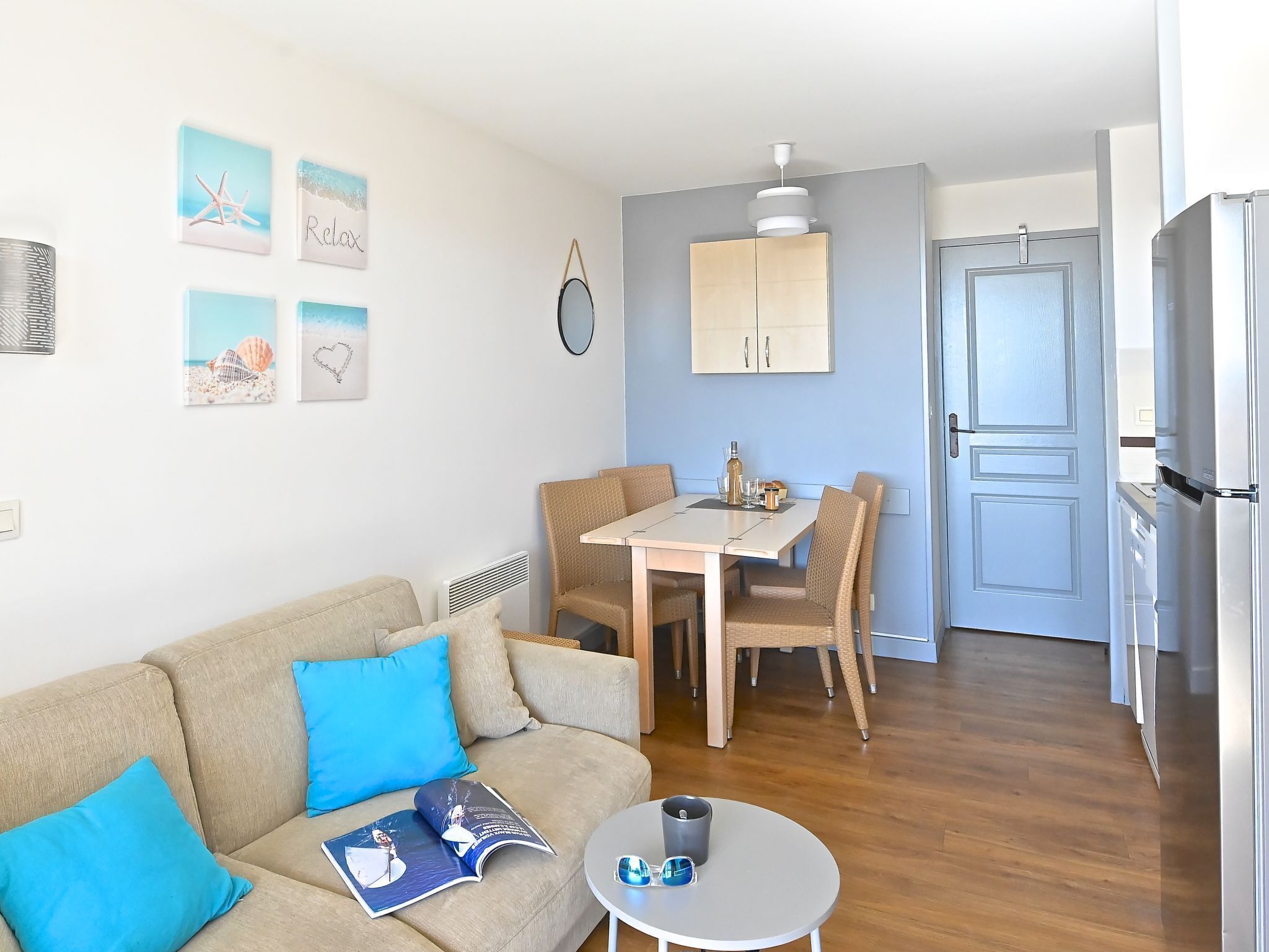 Un salon moderne avec un canapé beige, une table à manger avec des chaises et un coin cuisine équipé d’un réfrigérateur.