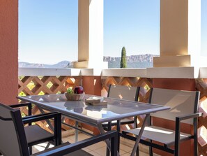 An outdoor patio with a table and chairs, a wicker basket with fruit, and a view of mountains. - Village Cap Estérel - L'Esquinade by Interhome (Agay Village Cap Esterel)