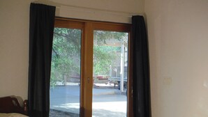 Una habitación con cama, ventana con cortinas y vista a la calle y árboles.