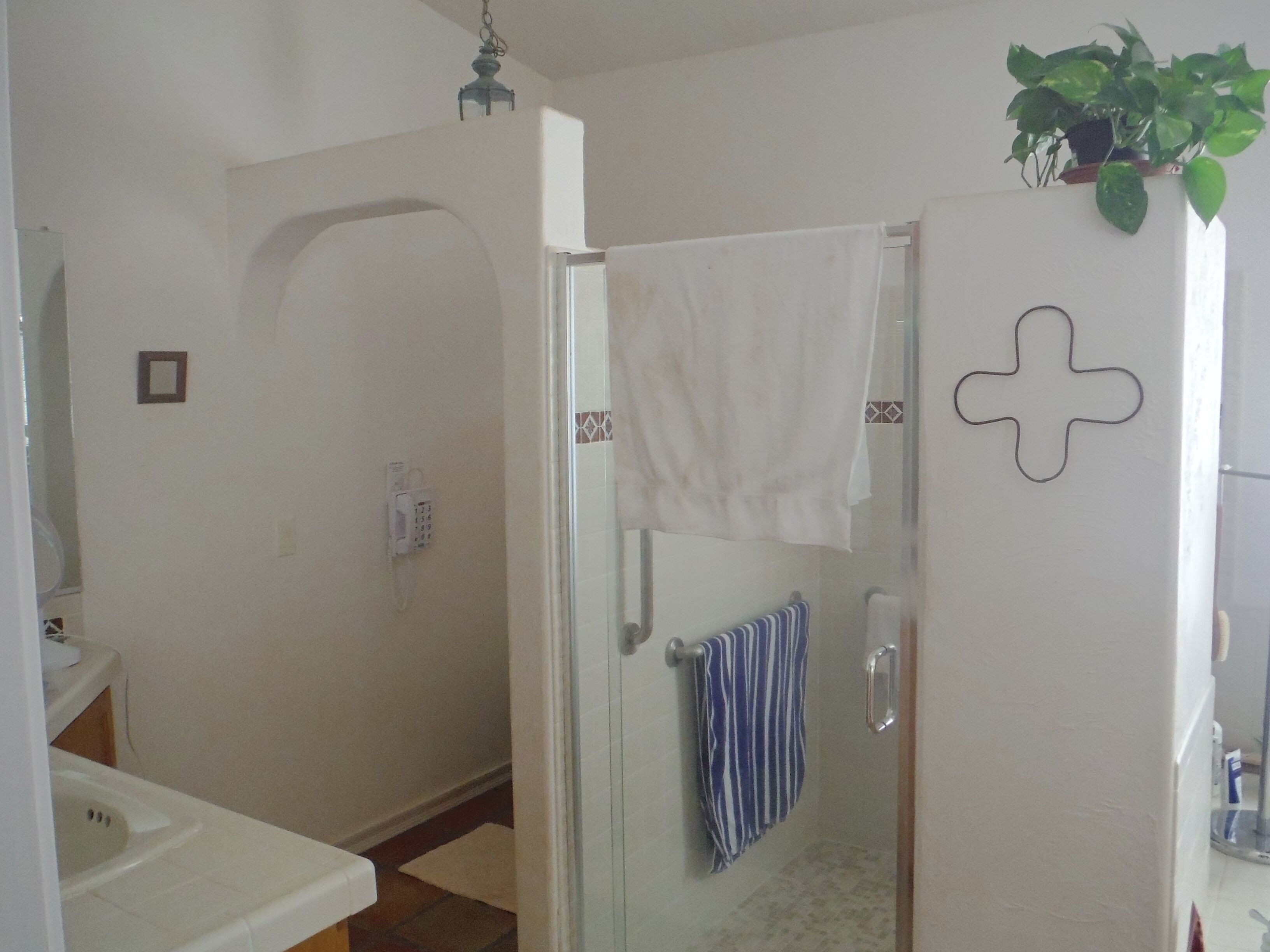Une salle de bain avec une douche, des toilettes et un lavabo. Une serviette est accrochée au mur et une plante est posée sur la porte.