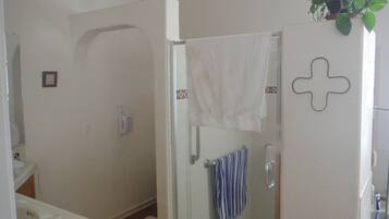 Une salle de bain avec une douche, des toilettes et un lavabo. Une serviette est accrochée au mur et une plante est posée sur la porte.