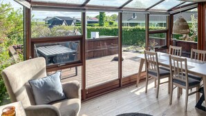 A sunroom with a wooden deck, a dining table with chairs, and a cushioned chair. - 2 bedroom nice home in Juelsminde (Juelsminde)