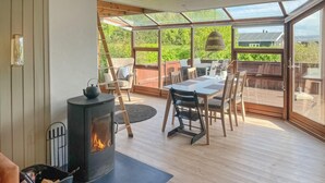 A cozy room with a wood-burning stove, a dining table with chairs, and a large glass door leading to an outdoor deck. - 2 bedroom nice home in Juelsminde (Juelsminde)