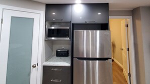 A compact kitchen with a stainless steel refrigerator, a microwave, and a toaster. - Separate Entrance Basement Suite (Winnipeg)