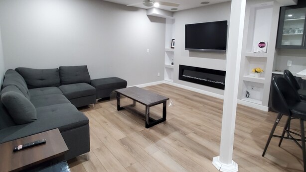 A modern living room with a sectional sofa, a coffee table, a TV mounted on the wall, and a fireplace. - Separate Entrance Basement Suite (Winnipeg)