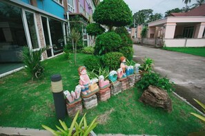 Uma rua residencial com casas, um gramado bem cuidado e uma fileira de figurinhas coloridas em um muro baixo.