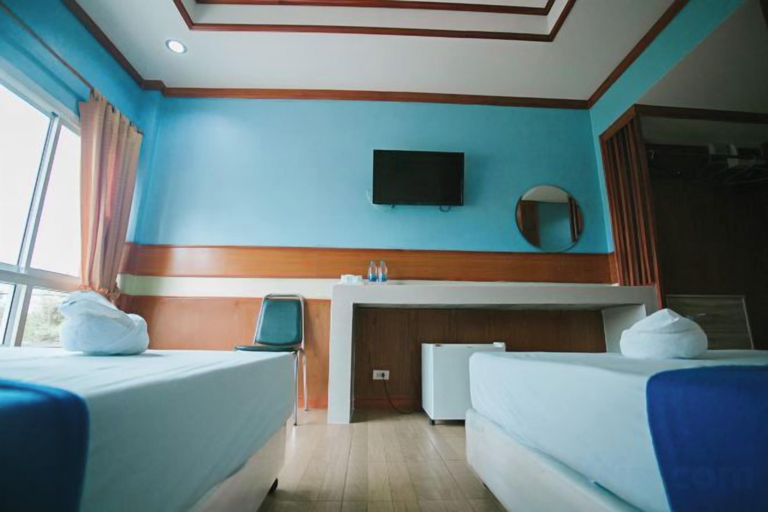 A hotel room with two beds, a flat-screen TV, a small desk, and a window.