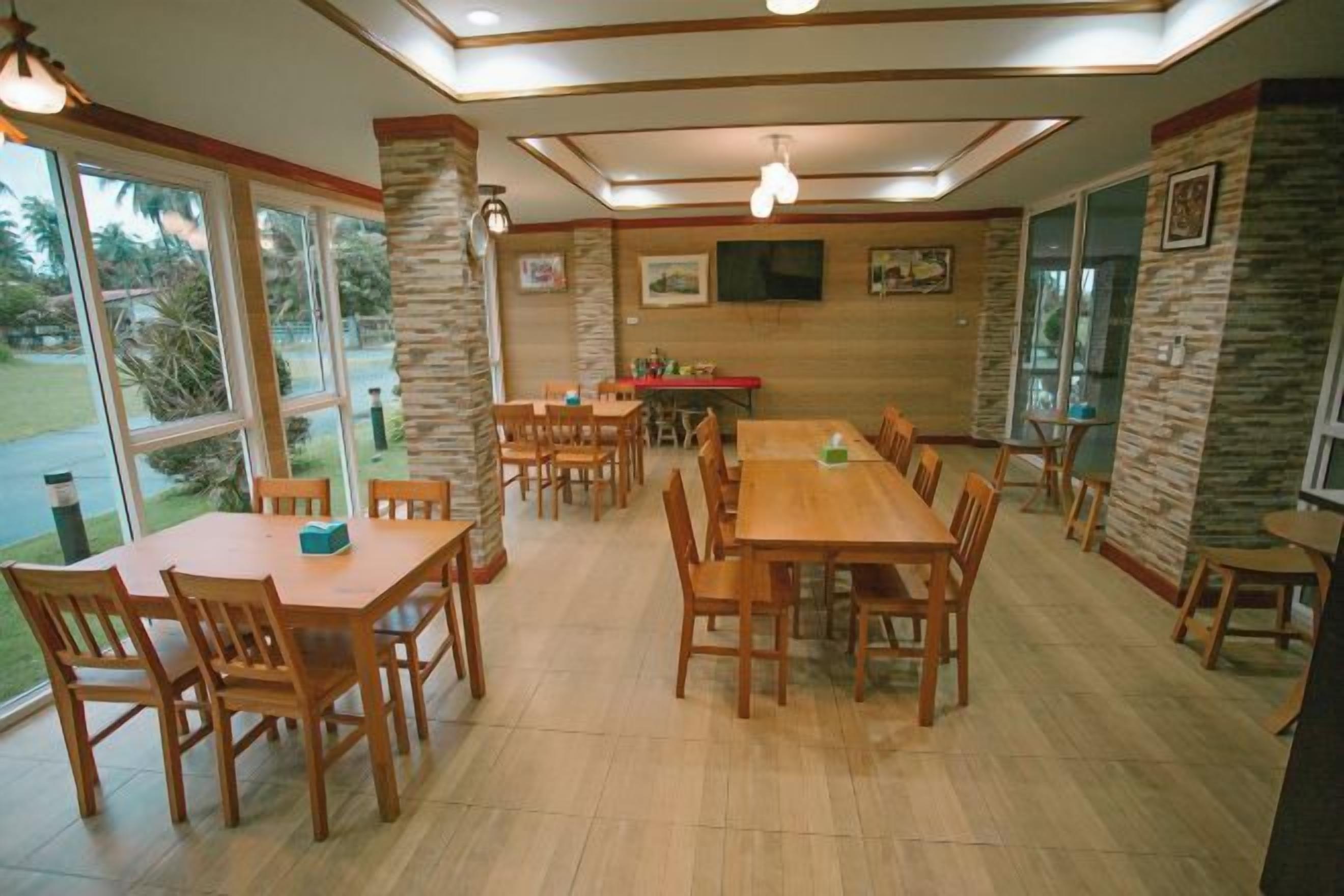 A dining area with multiple wooden tables and chairs, stone accent walls, and large windows offering a view of the outdoors.