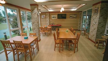A dining area with multiple wooden tables and chairs, stone accent walls, and large windows offering a view of the outdoors.