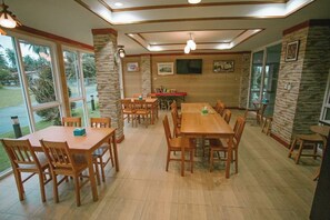 A dining area with multiple wooden tables and chairs, stone accent walls, and large windows offering a view of the outdoors. - T.W. Sea View Hotel (Tha Sala)