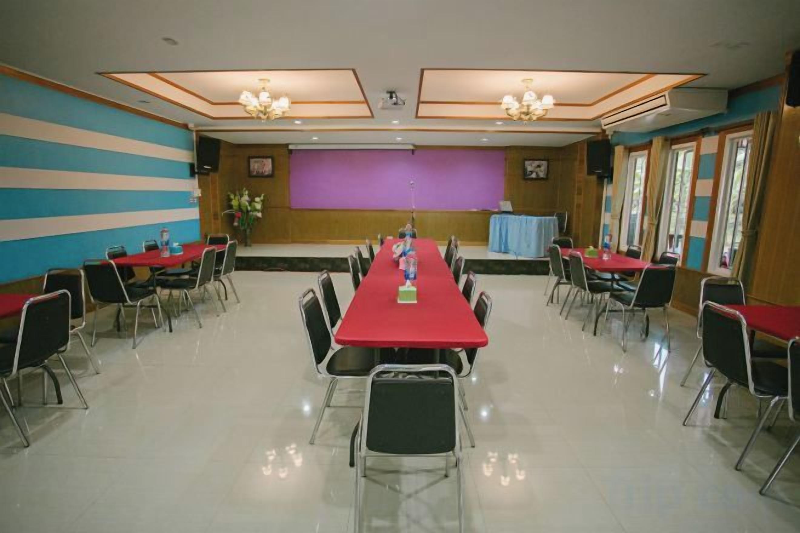 Un salón de conferencias con una larga mesa, sillas, un escenario y una pantalla de proyección.