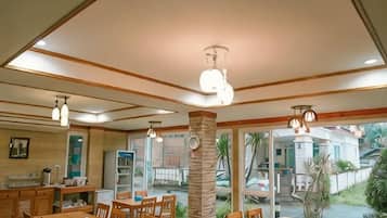 Un espace repas avec des tables et des chaises en bois, un coin cuisine avec des placards et une vue sur l’extérieur.