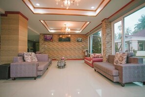 A spacious living room with sofas, a chandelier, and a stone wall. - T.W. Sea View Hotel (Tha Sala)
