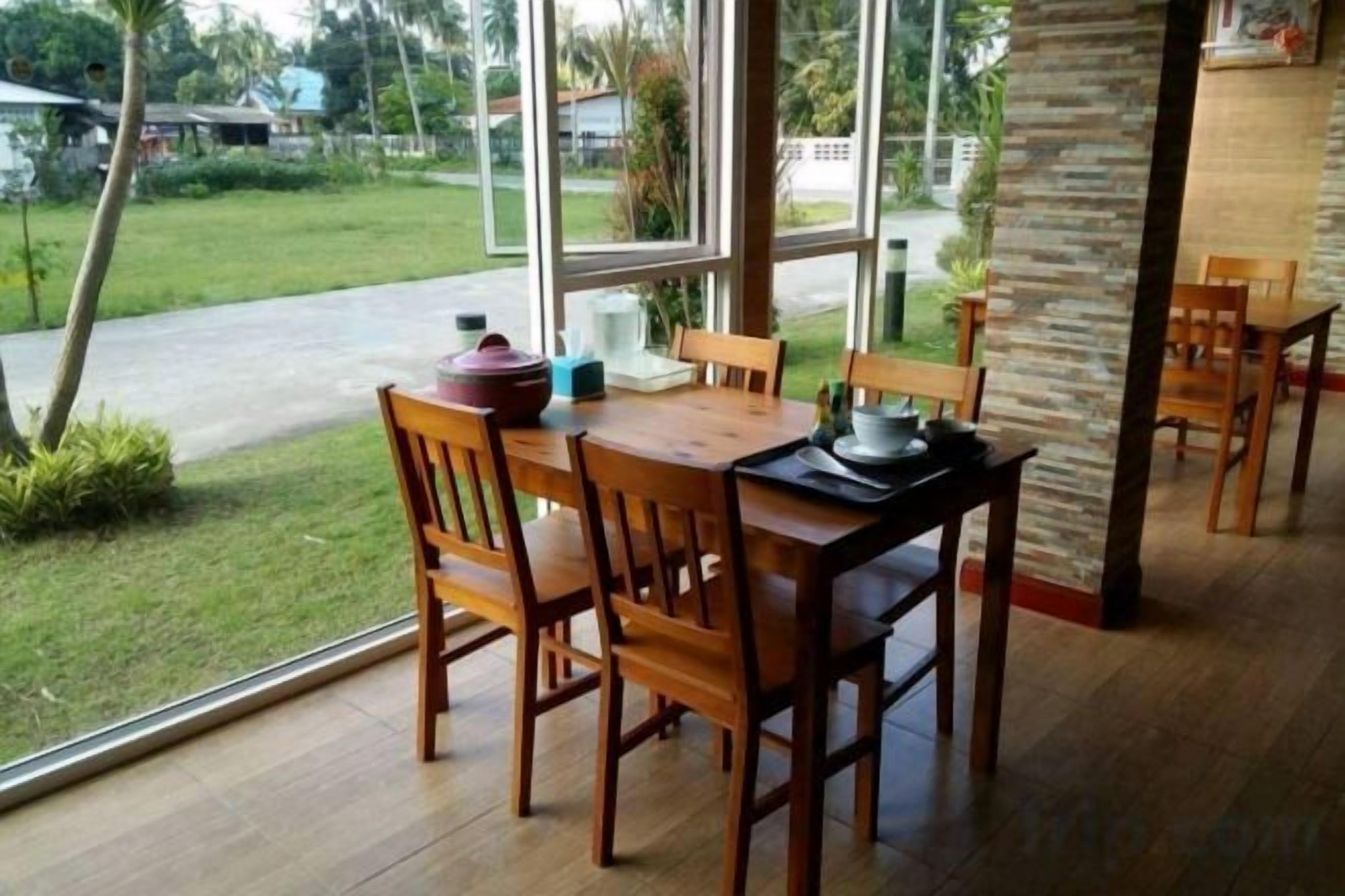 A wooden dining table with chairs, a stone pillar, and a view of a green landscape through large windows.