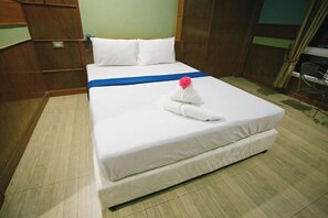 Una cama bien hecha con una colcha azul, una almohada blanca y una toalla doblada con una flor roja.
