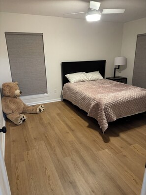 Ein Schlafzimmer mit einem Bett, einem Nachttisch mit Lampe, einem Deckenventilator und einem Teddybären auf dem Boden.