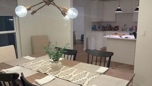 Ein Essbereich mit Holztisch, schwarzen Stühlen, einer gewebten Tischmatte und einer Pendelleuchte.